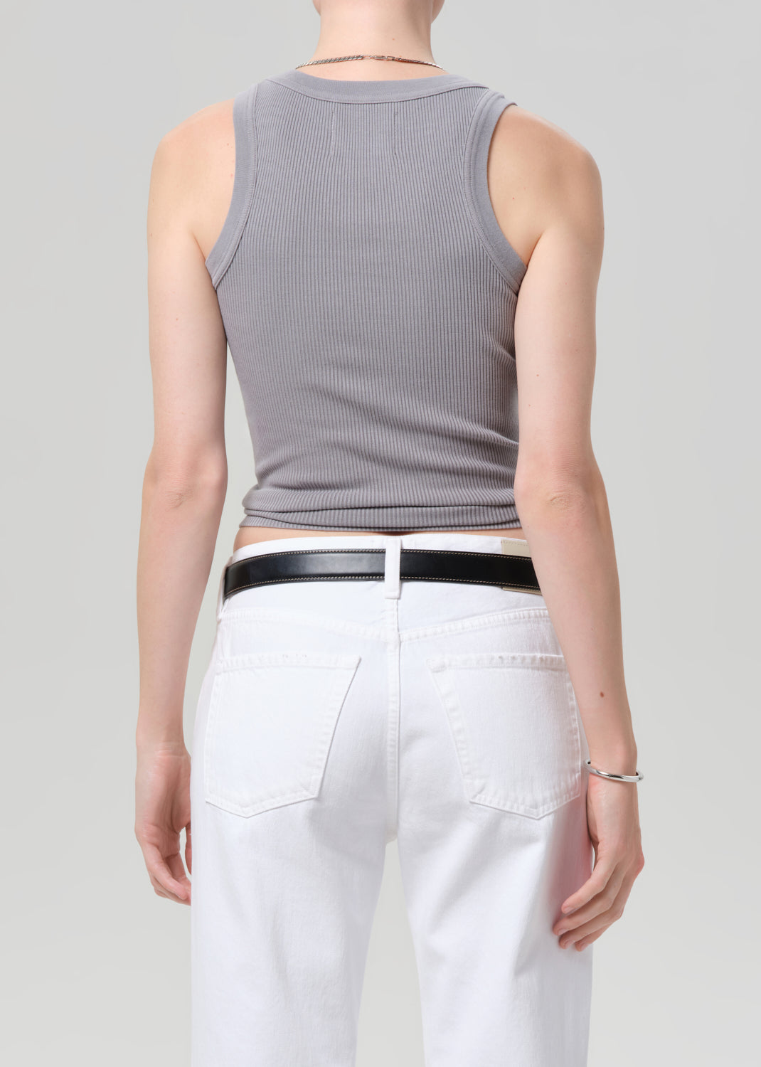 Person wearing a gray sleeveless top and white pants on a plain background