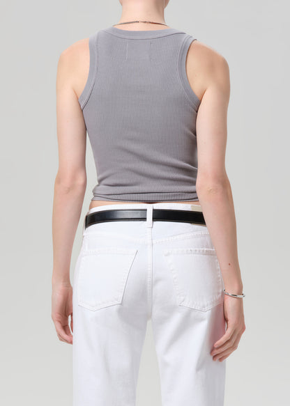 Person wearing a gray sleeveless top and white pants on a plain background