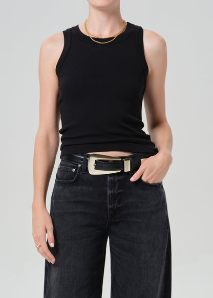 Person wearing a black sleeveless top and black pants with a gold belt on a light gray background