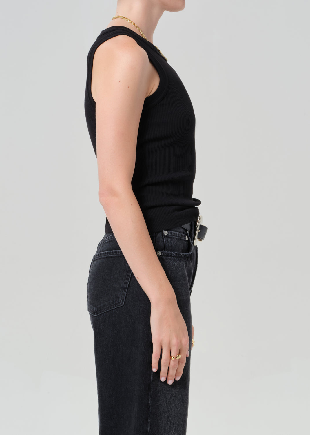 Person wearing a black sleeveless top and black jeans on a light gray background