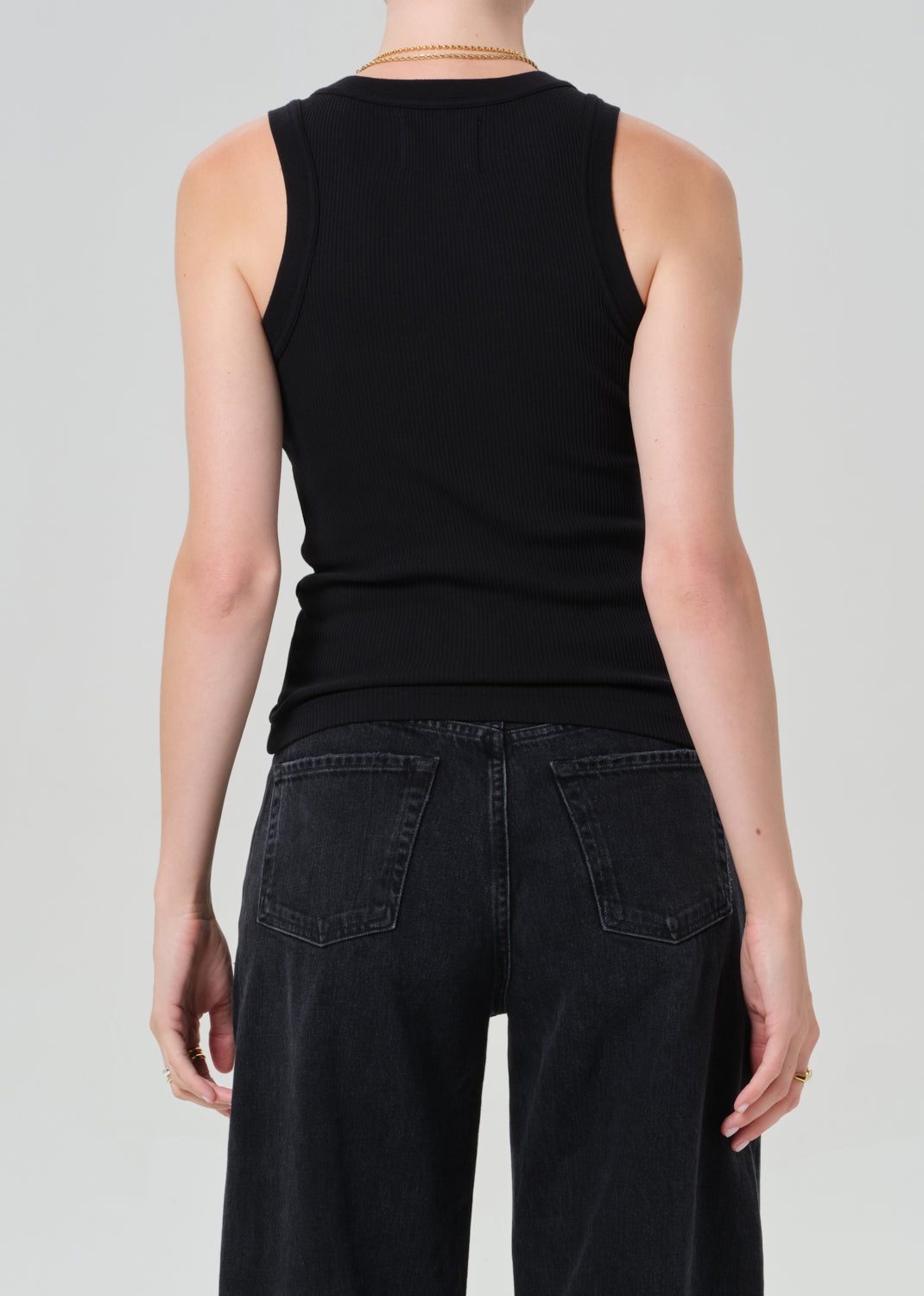 Person wearing a black sleeveless top and black pants on a light gray background