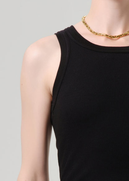 Close-up of a person wearing a black ribbed sleeveless tank top and a gold chain necklace against a grey background.