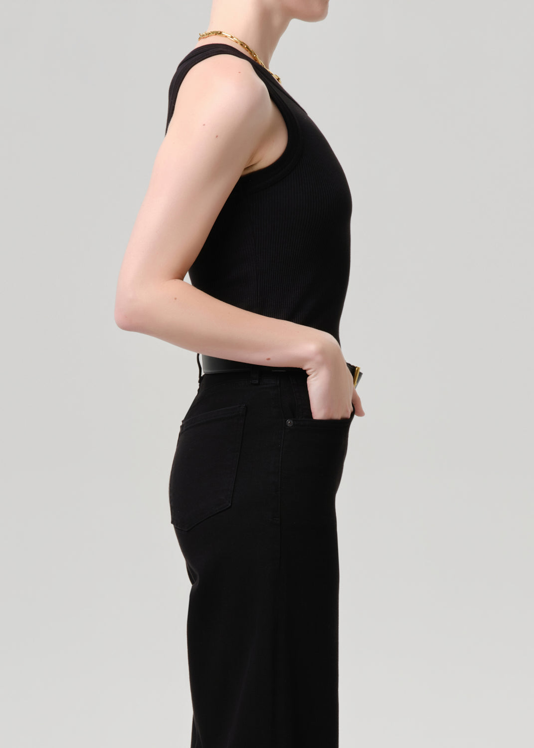Side profile of a model wearing a black sleeveless top and black wide-leg trousers against a grey background.
