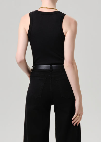 A model shown from the back wearing a black sleeveless top and black wide-leg pants, paired with a black belt and gold jewelry, against a grey background.