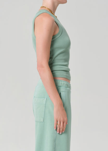 Person wearing a green ribbed tank top and pants on a light gray background