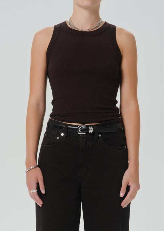 A model wearing a dark brown ribbed sleeveless crop top paired with black jeans and a black belt, shown from the neck down against a grey background.