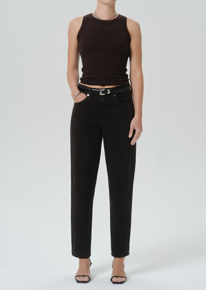 A model wearing a dark brown ribbed sleeveless crop top, black straight-leg jeans with a black belt, and black heeled sandals, photographed against a grey background.