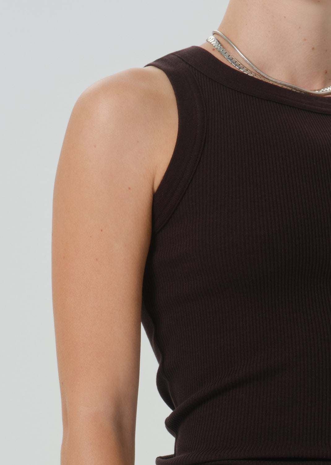 Close-up of a model wearing a dark brown ribbed sleeveless top against a grey background.
