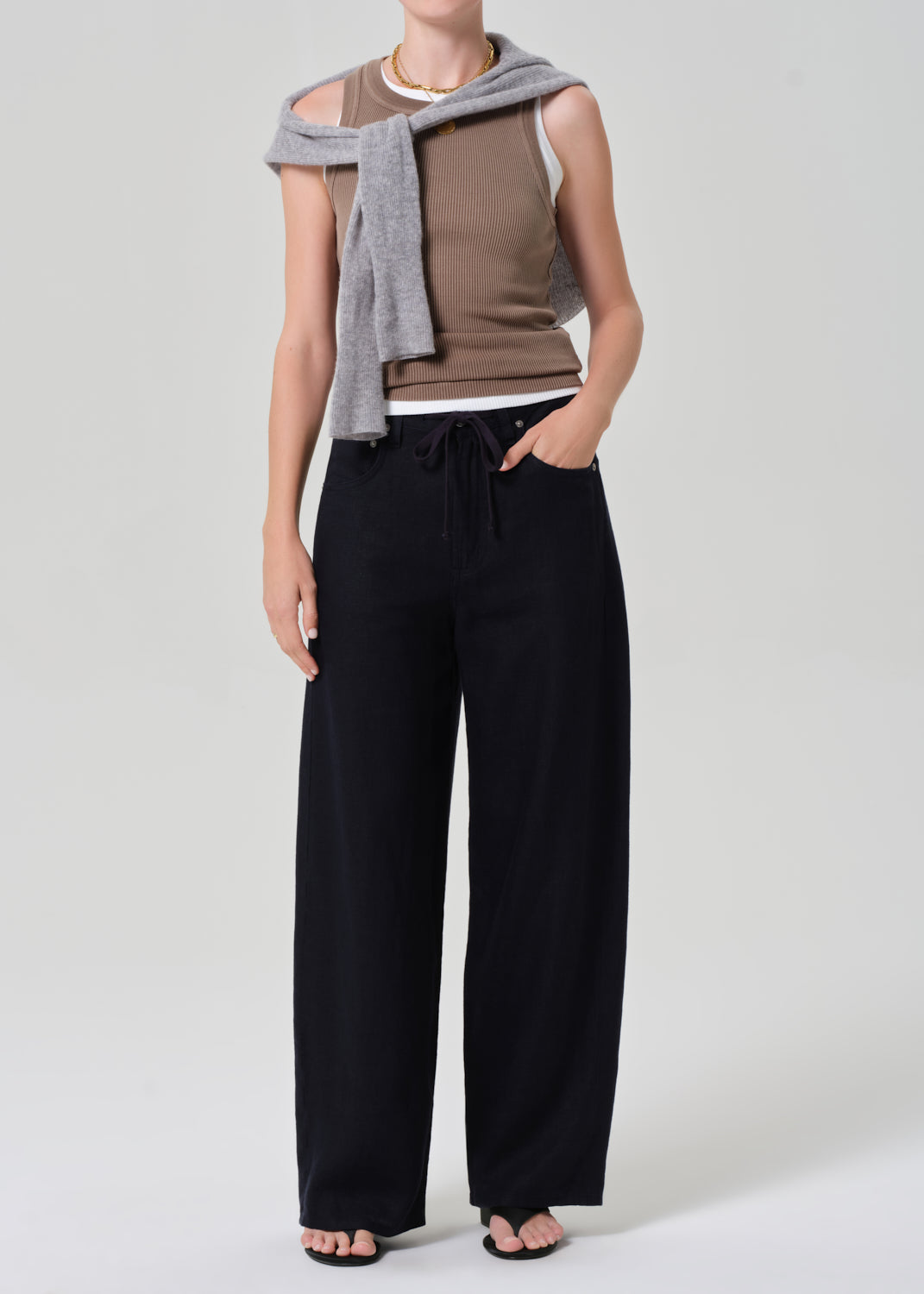 Person wearing a brown ribbed tank and navy pants on a gray background