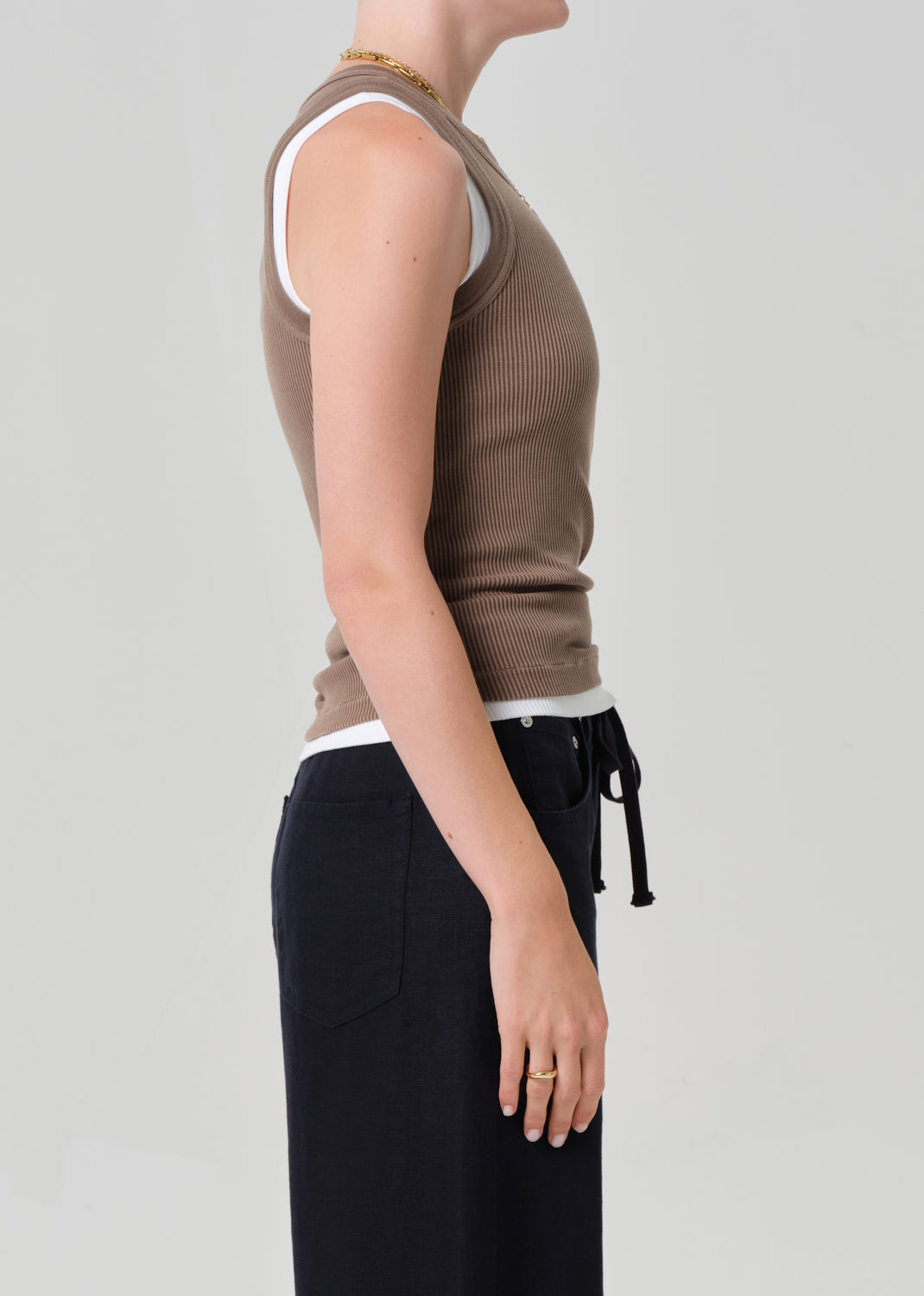 Person wearing a brown ribbed tank and navy pants on a gray background