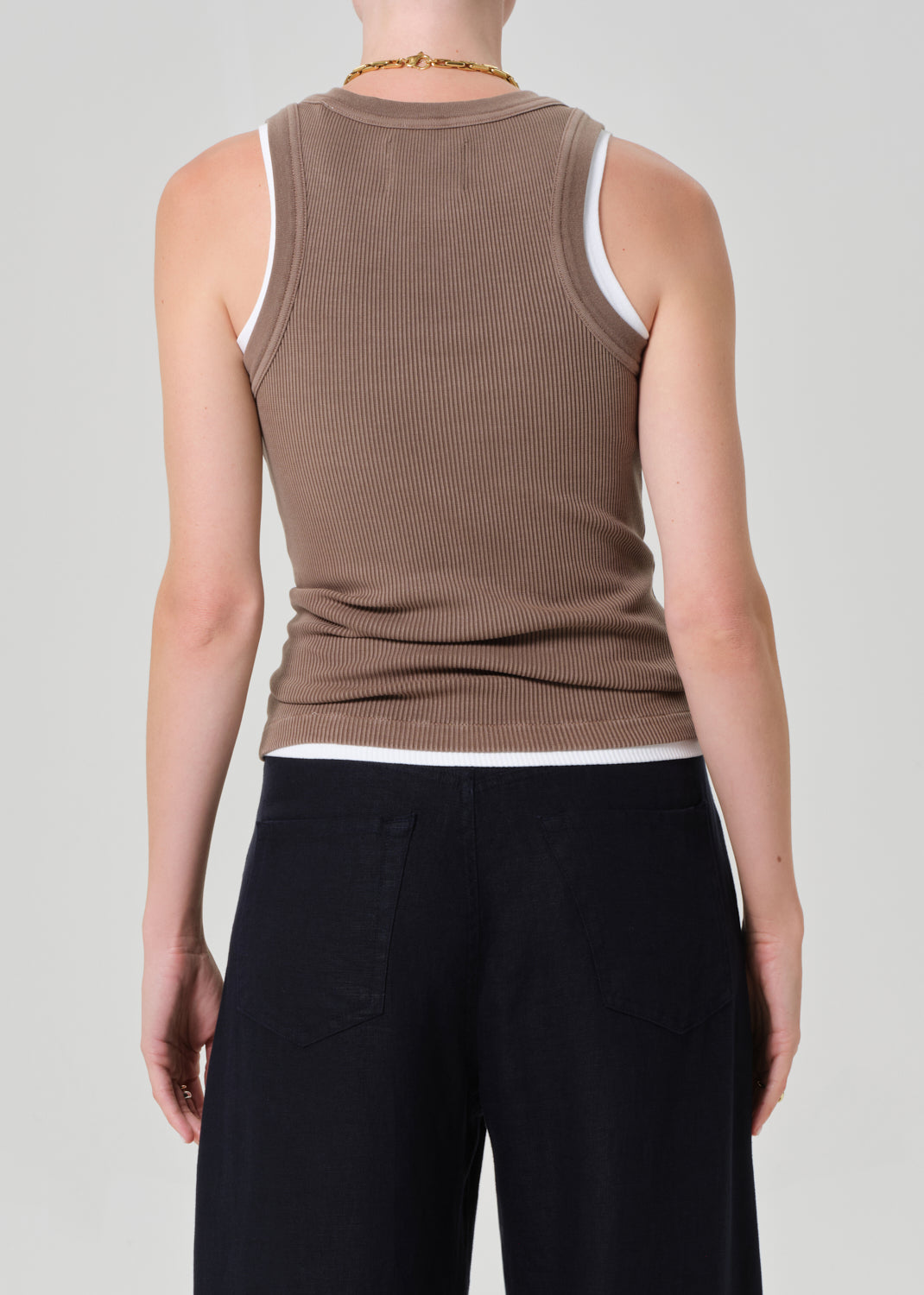 Person wearing a brown ribbed tank and navy pants on a gray background