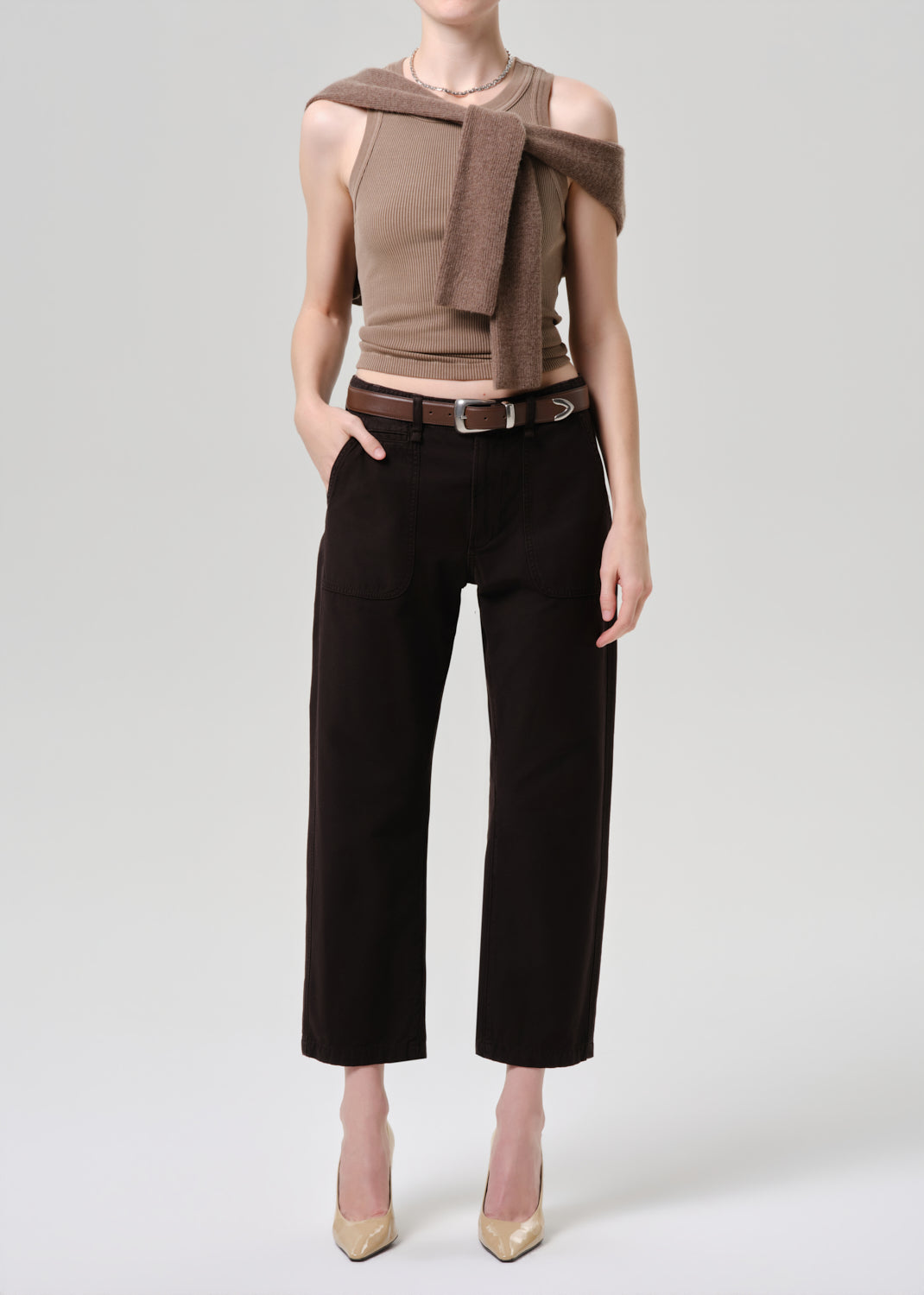 Person wearing a brown top and black pants on a grey background.