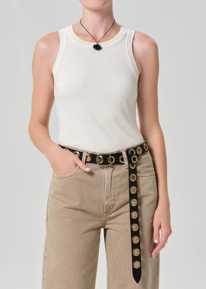 Person wearing a white sleeveless top and beige pants with a decorative belt on a plain background