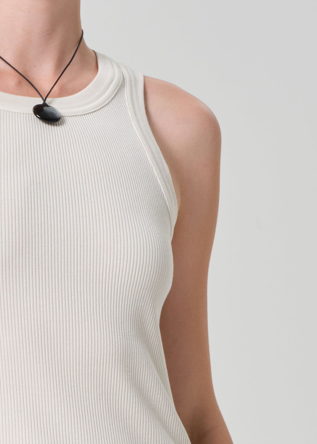 Person wearing a white sleeveless top and black necklace on a plain background