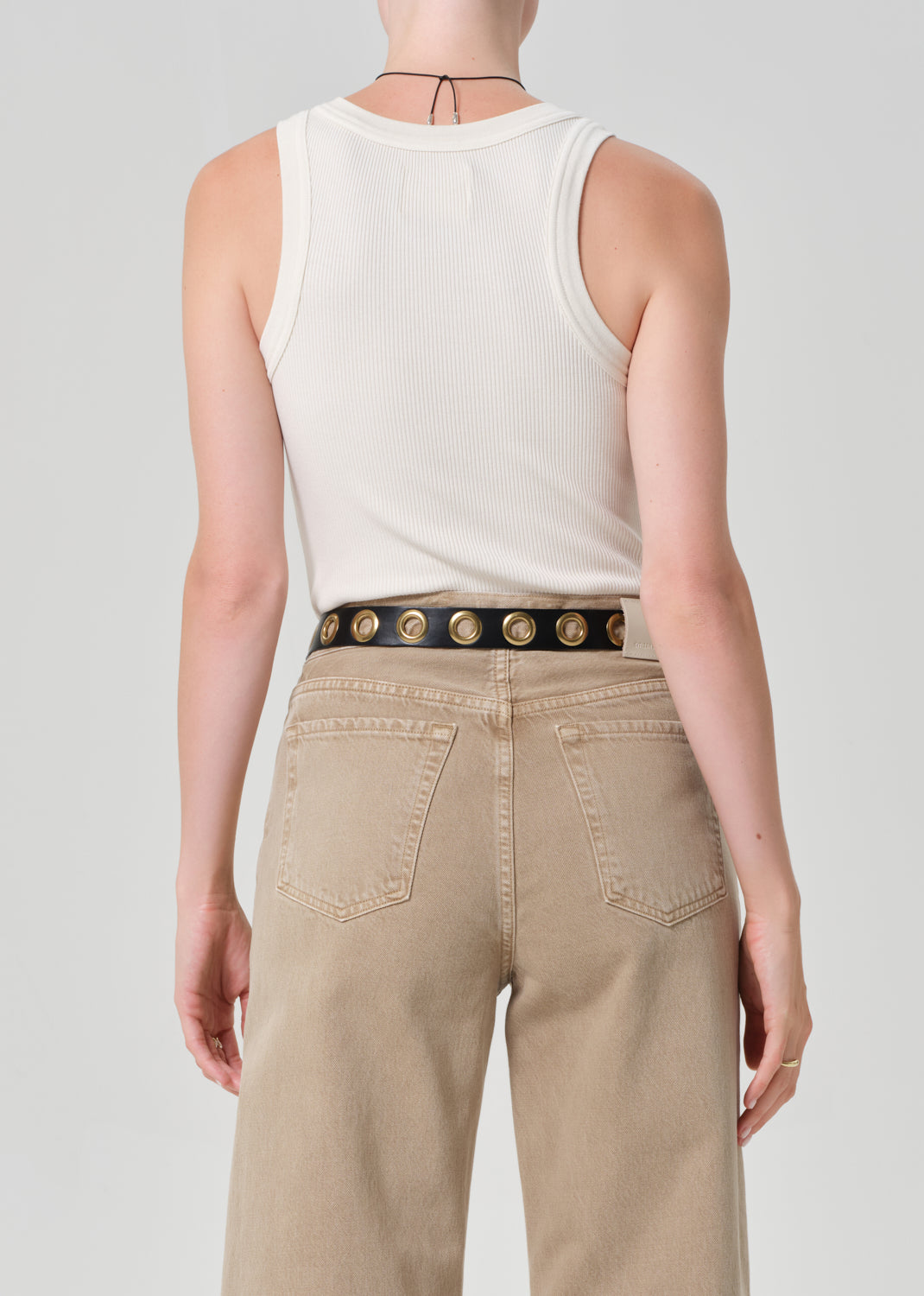 Person wearing a white tank top and beige pants with a decorative belt on a plain background