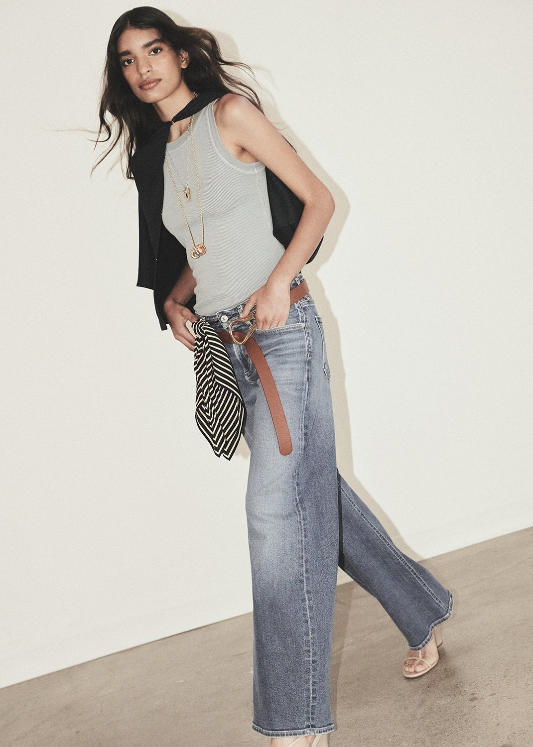 Woman wearing a grey sleeveless and blue jeans with a white background