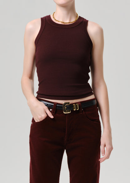 A model wearing a sleeveless ribbed knit top in deep burgundy, paired with matching burgundy pants and a black belt with a gold buckle, against a grey background.