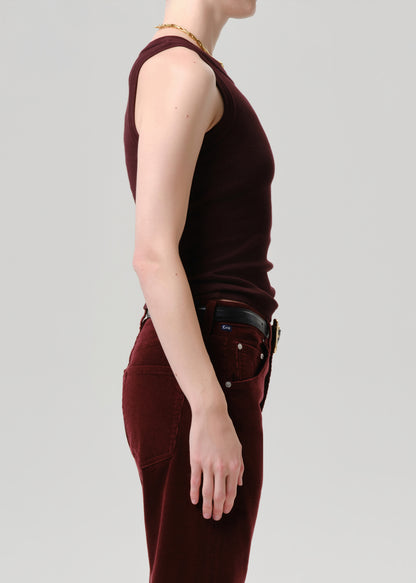 Side profile of a model wearing a sleeveless, fitted burgundy top and matching burgundy pants, styled with a black belt and gold jewelry against a grey background.