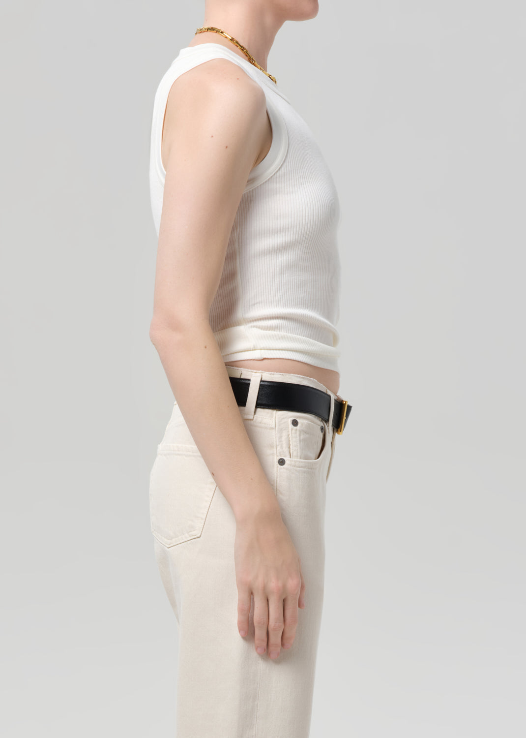 Person wearing a white sleeveless top and beige pants on a light gray background