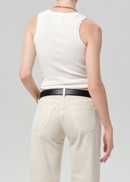 Person wearing a white sleeveless top and beige pants with a black belt on a light gray background