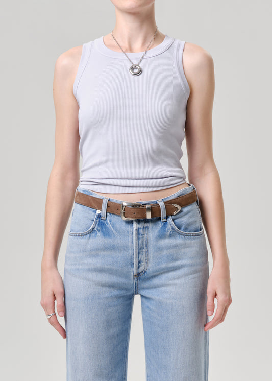 Person wearing a light blue tank top and light blue jeans with a brown belt on a grey background