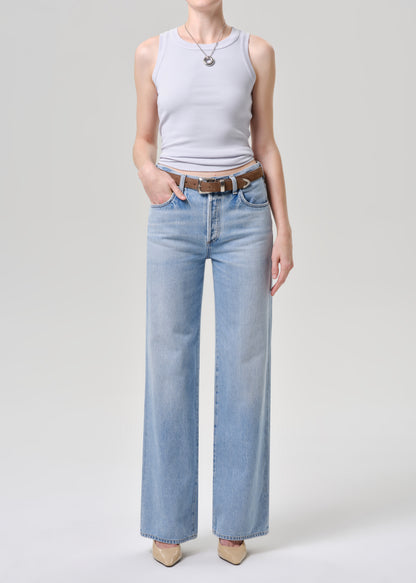 Person wearing a light blue tank top and light blue jeans on a blue background