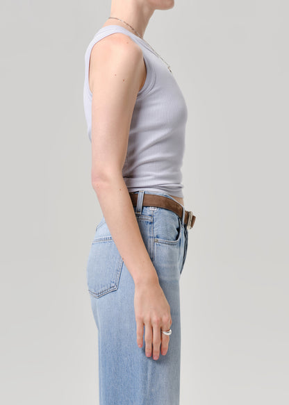 Person wearing a light blue tank top and blue jeans on a grey background