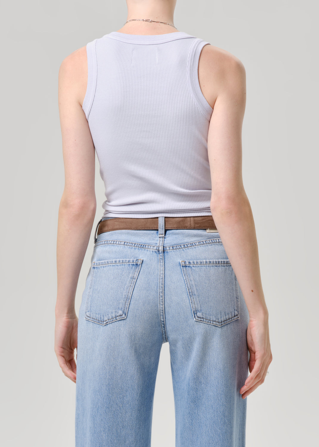 Person wearing a light blue tank top and light blue jeans on a grey background
