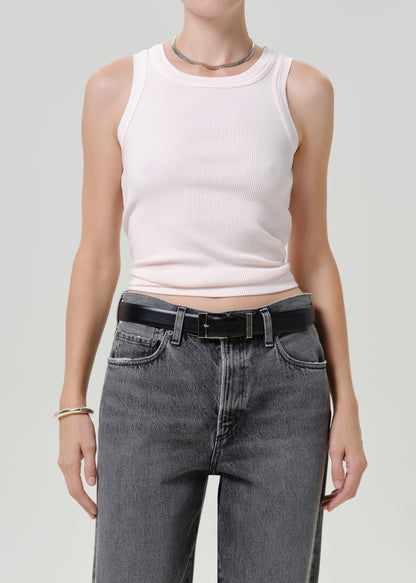 A model wearing a light pink ribbed tank top and high-waisted gray jeans with a black belt, shown from the neck down against a light gray studio background.