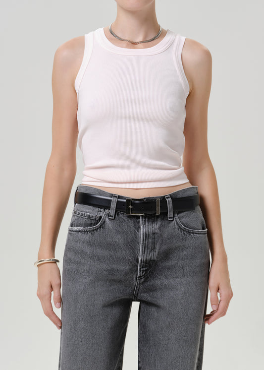 A model wearing a light pink ribbed tank top and high-waisted gray jeans with a black belt, shown from the neck down against a light gray studio background.