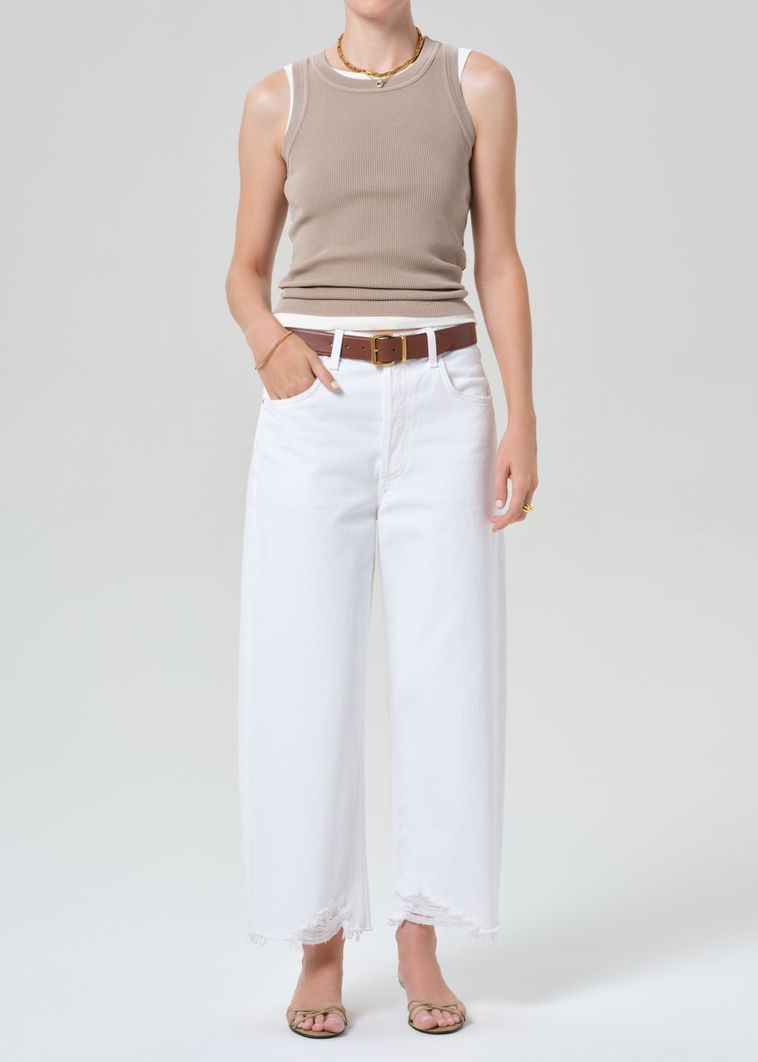 Person wearing a beige sleeveless top and white pants on a plain background