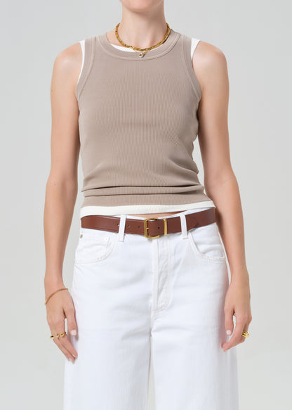 Person wearing a beige sleeveless top and white pants with a brown belt on a plain background