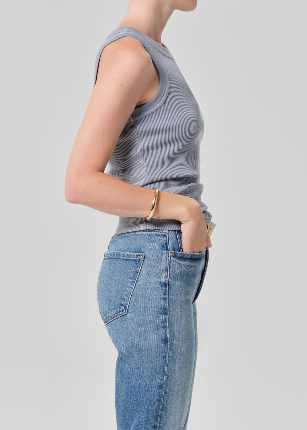 Person wearing a light grey ribbed tank top and jeans on a plain background