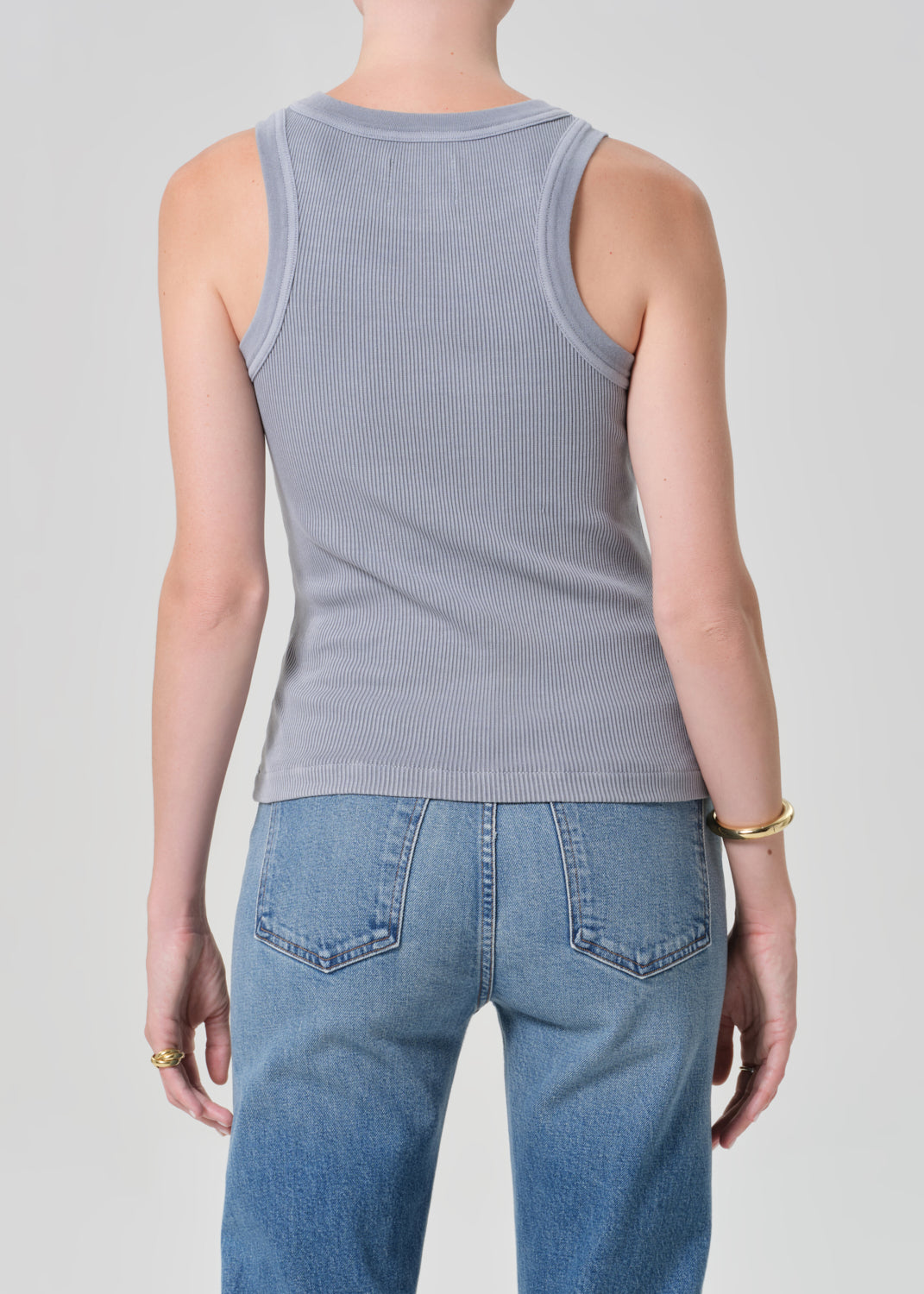 Person wearing a gray ribbed tank top and blue jeans on a plain background