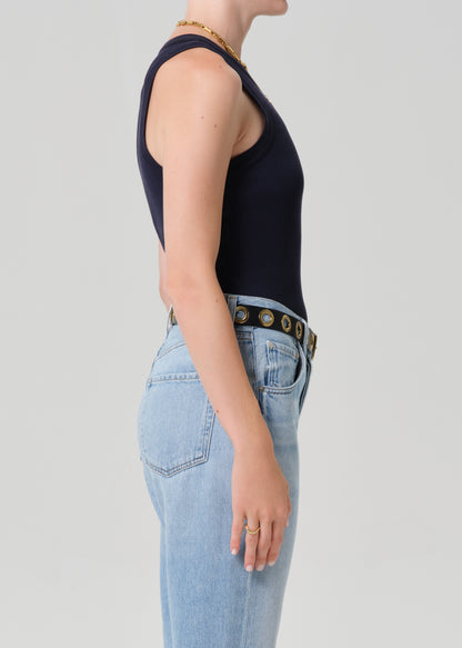 Person wearing a navy sleeveless top and light blue jeans with a decorative belt on a gray background