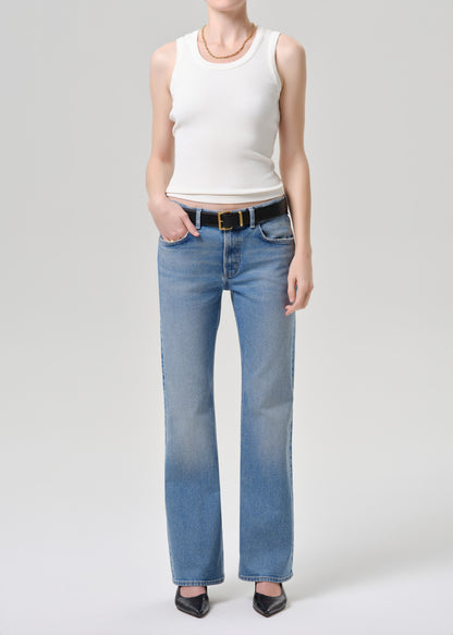 A model wearing light-wash blue straight-leg jeans with a black belt, paired with a white ribbed tank top and black pointed-toe heels, photographed against a grey background.