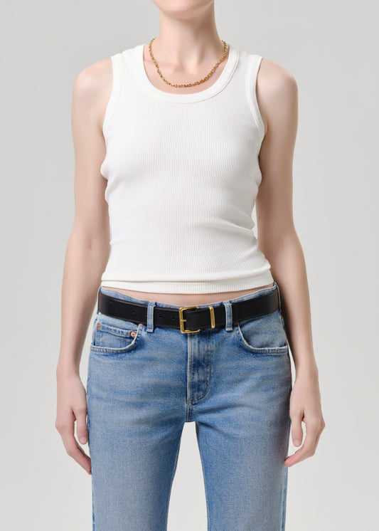 A model wearing a white ribbed tank top and light blue jeans with a black belt, shown from the neck down against grey background.
