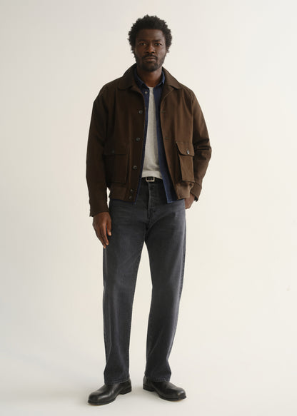 Person wearing washed charcoal grey straight leg jeans with a dark brown jacket, dark shirt, and black shoes, front full body view on a light grey background.