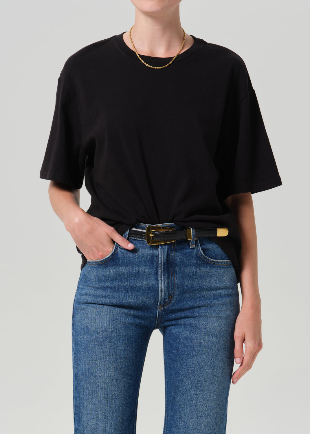 Person wearing black t-shirt with blue pants on a grey background