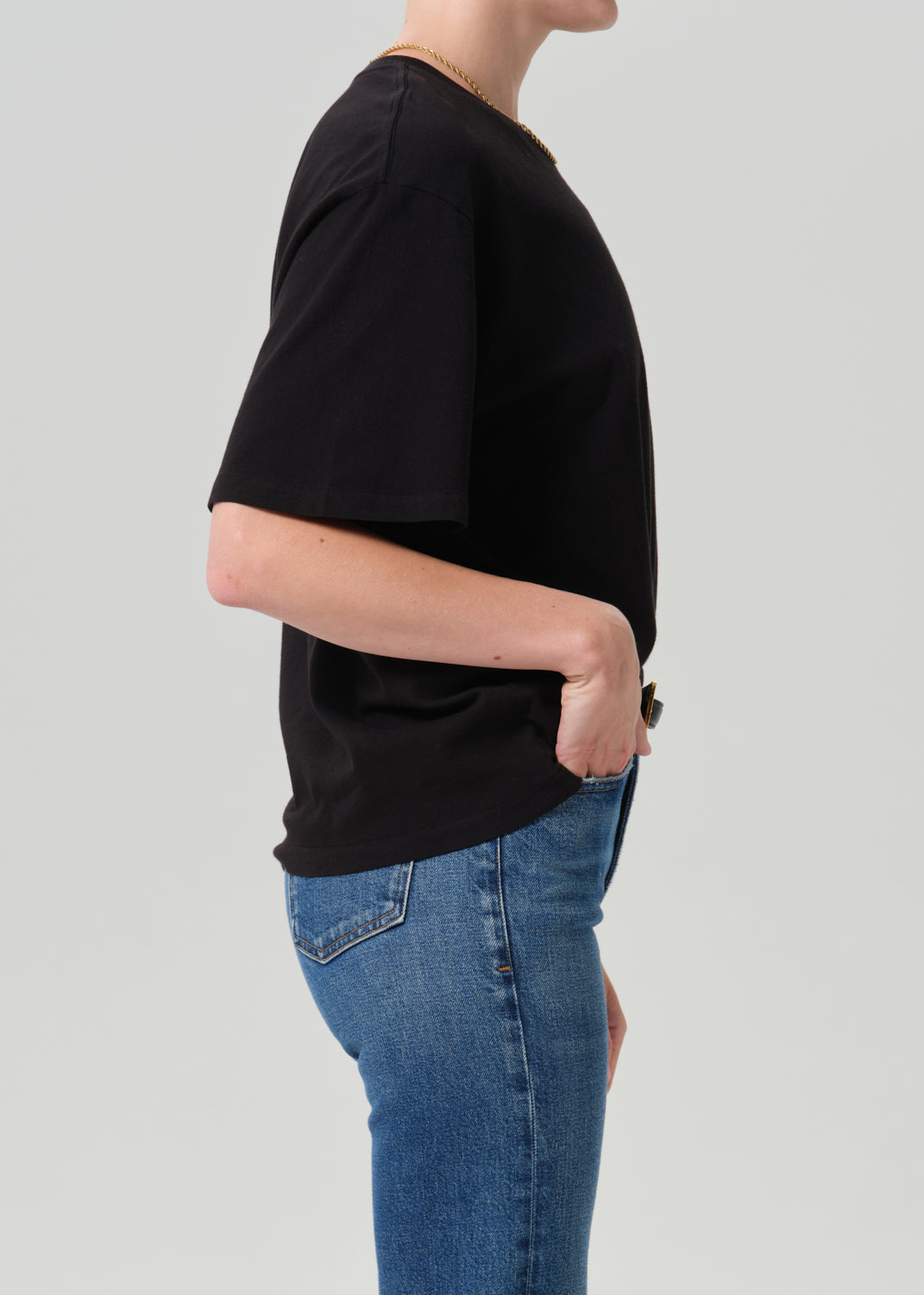 Person wearing black t-shirt with blue pants on a grey background