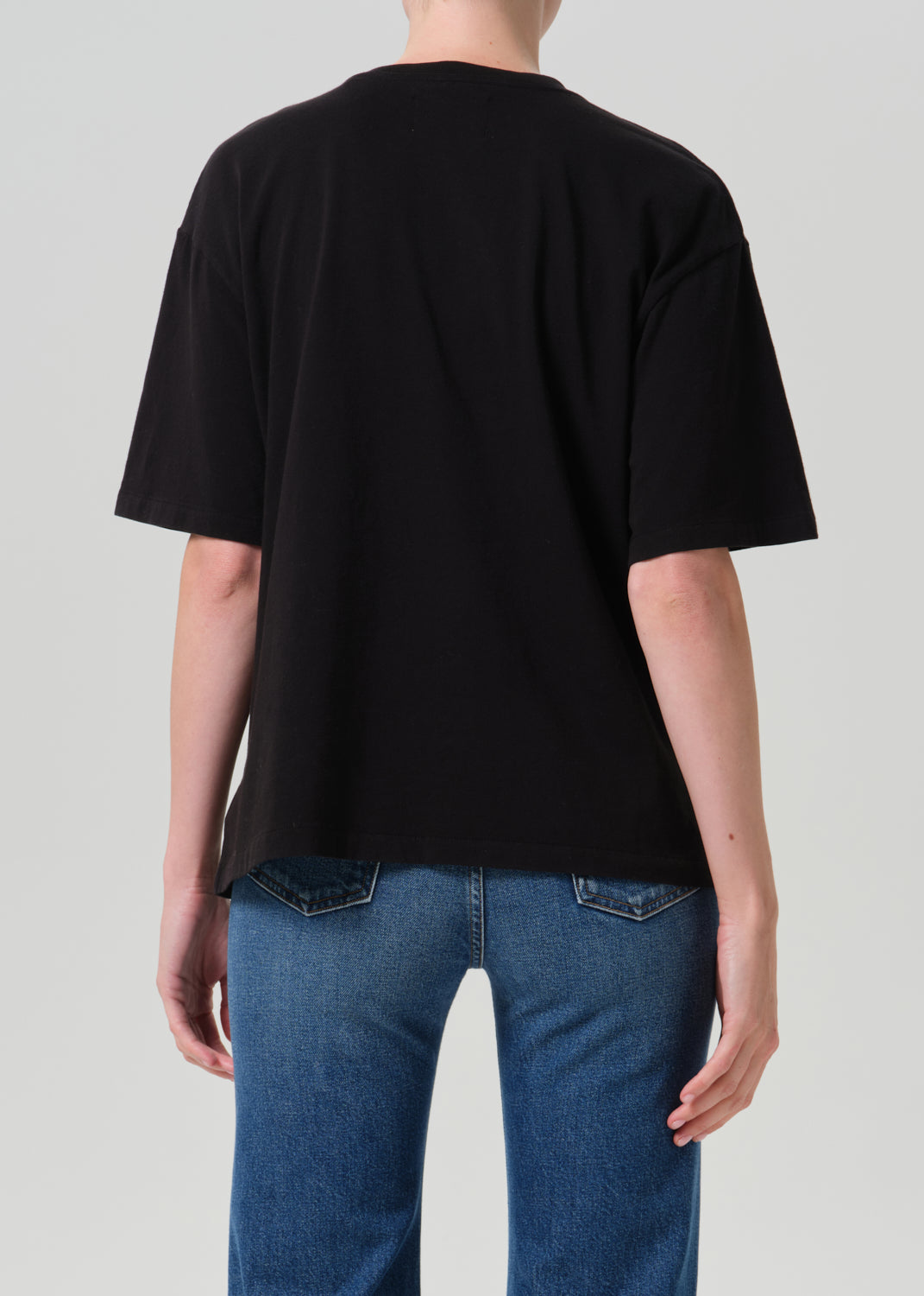 Person wearing black t-shirt with blue pants on a grey background