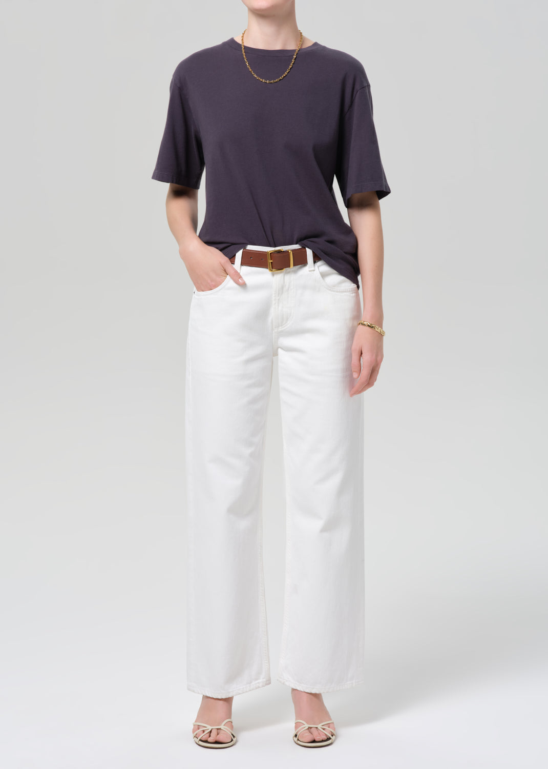 Person wearing a charcoal t-shirt and white pants with a plain background