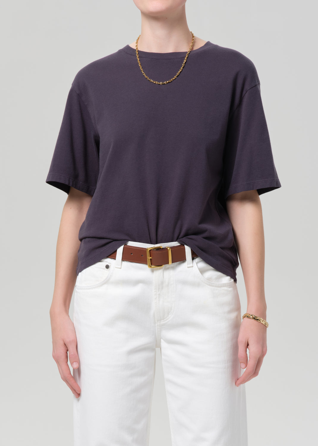 Person wearing a charcoal t-shirt and white pants with a plain background