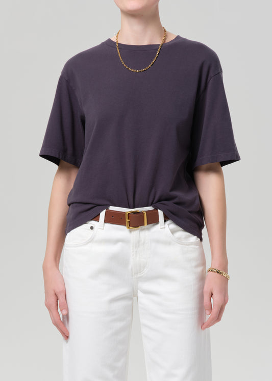 Person wearing a charcoal t-shirt and white pants with a plain background