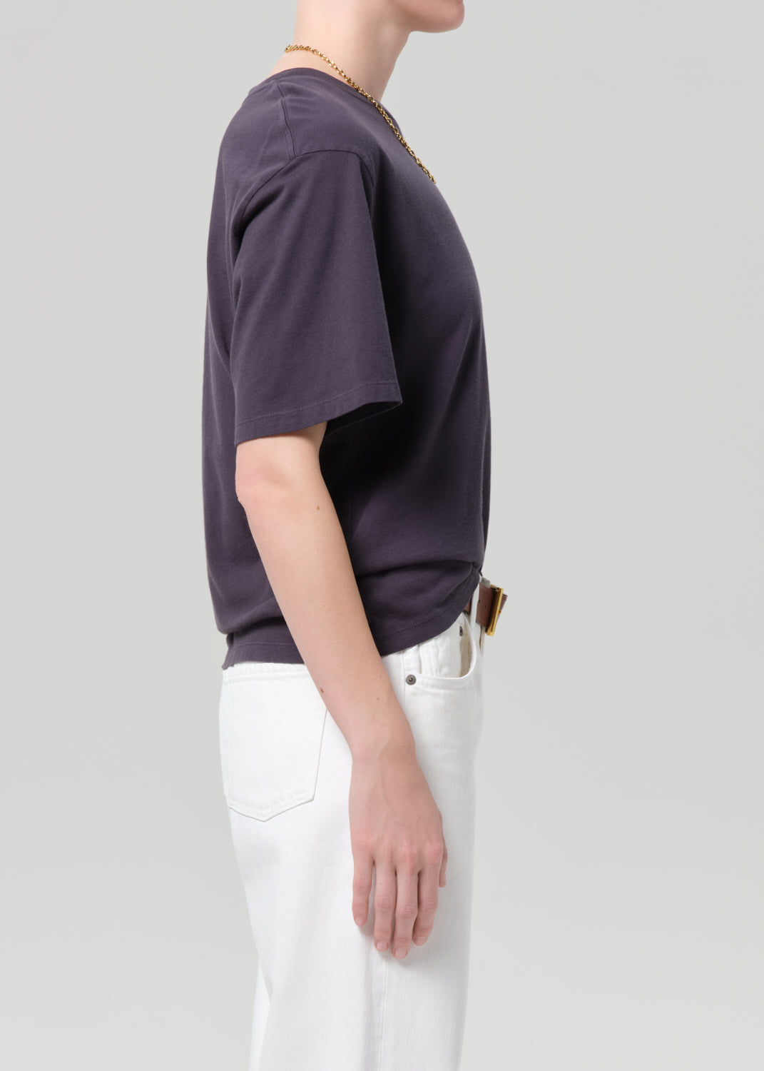 Person wearing a charcoal t-shirt and white pants with a plain background