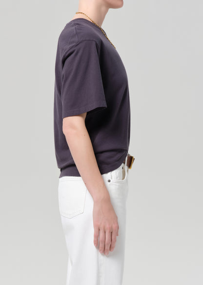 Person wearing a charcoal t-shirt and white pants with a plain background