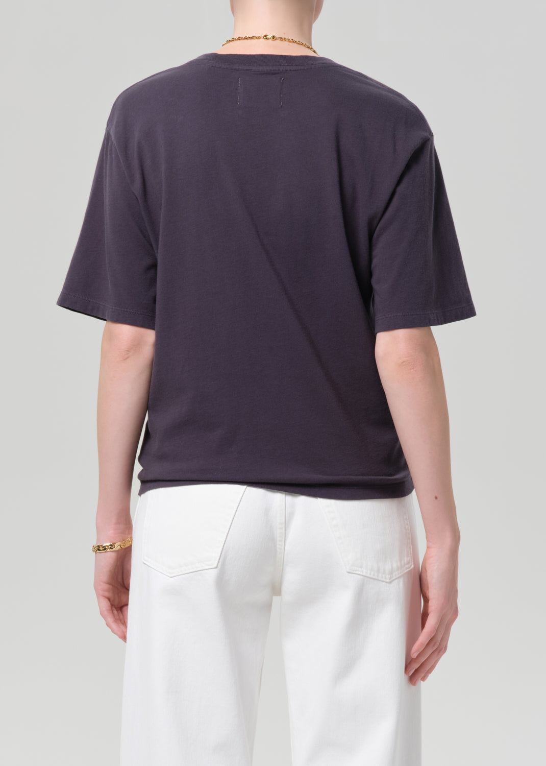 Person wearing a charcoal t-shirt and white pants with a plain background