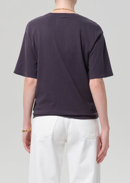 Person wearing a charcoal t-shirt and white pants with a plain background