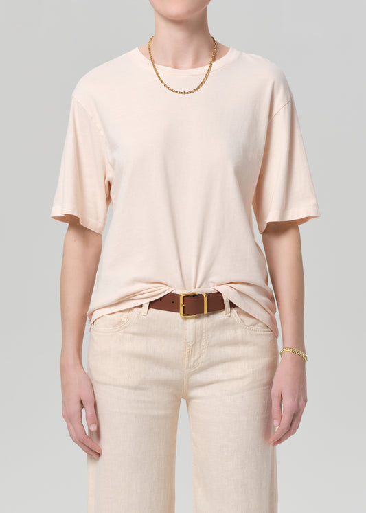 Person wearing a light pink t-shirt and beige pants with a belt on a plain background