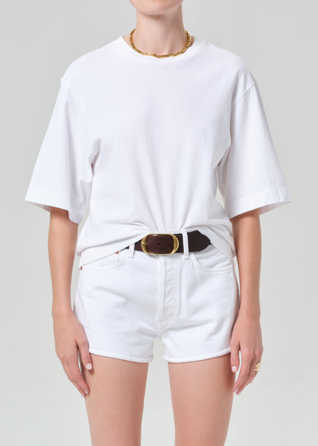 Person wearing a white t-shirt and white shorts with a belt on a plain background